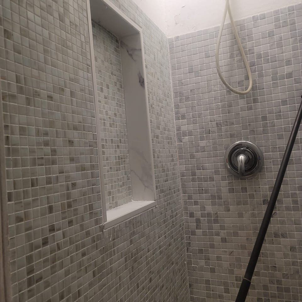 A remodeled tile shower with a marble accent niche